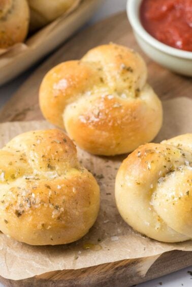 Close up of sourdough discard garlic knots on a wood serving tray with pizza sauce.