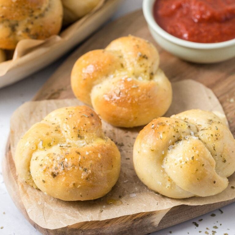 Close up of sourdough discard garlic knots on a wood serving tray with pizza sauce.