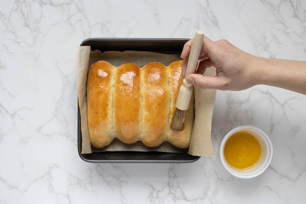 Brushing the buns with honey butter right after baking to make the sourdough discard iced buns.
