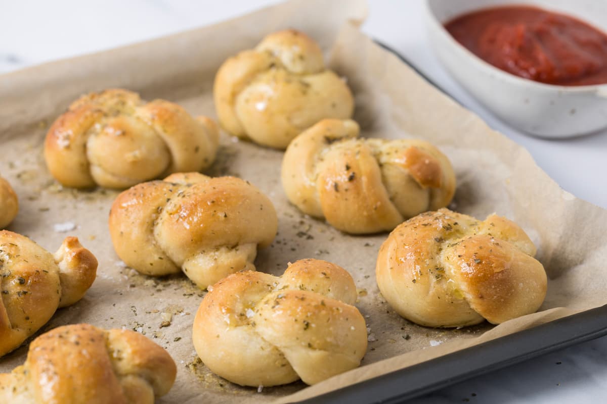 Fresh baked sourdough discard garlic knots on a baking sheet ready to serve with marinara sauce.