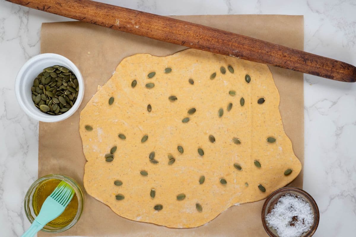 Pressing pumpkin seeds into rolled out dough to make sourdough pumpkin crackers.