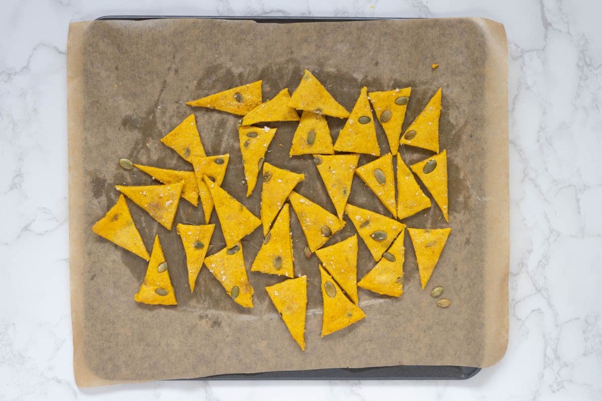 Fresh baked triangle shaped sourdough pumpkin crackers on a parchment lined baking sheet.