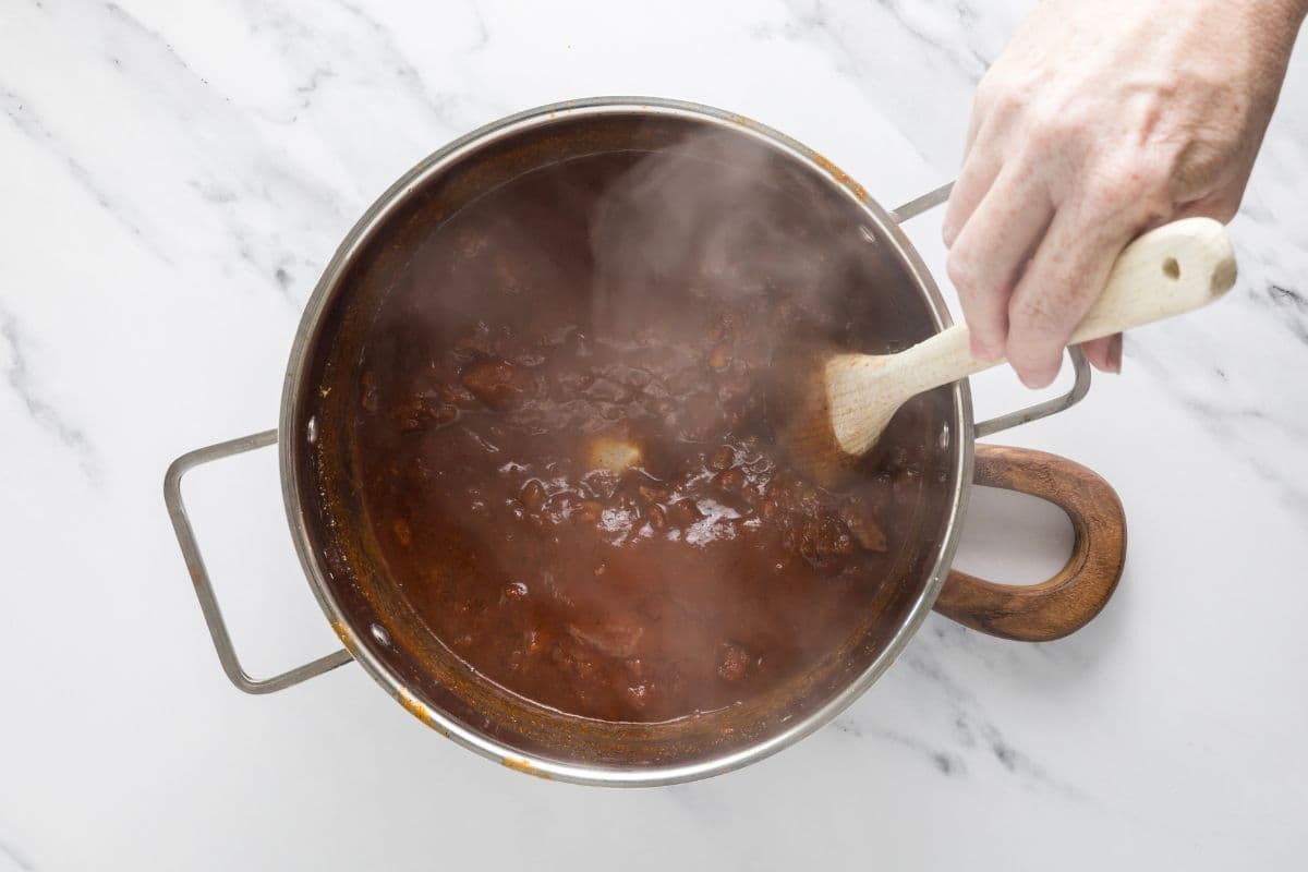 Simmering and stirring the ingredients in a pot to make homemade ketchup.