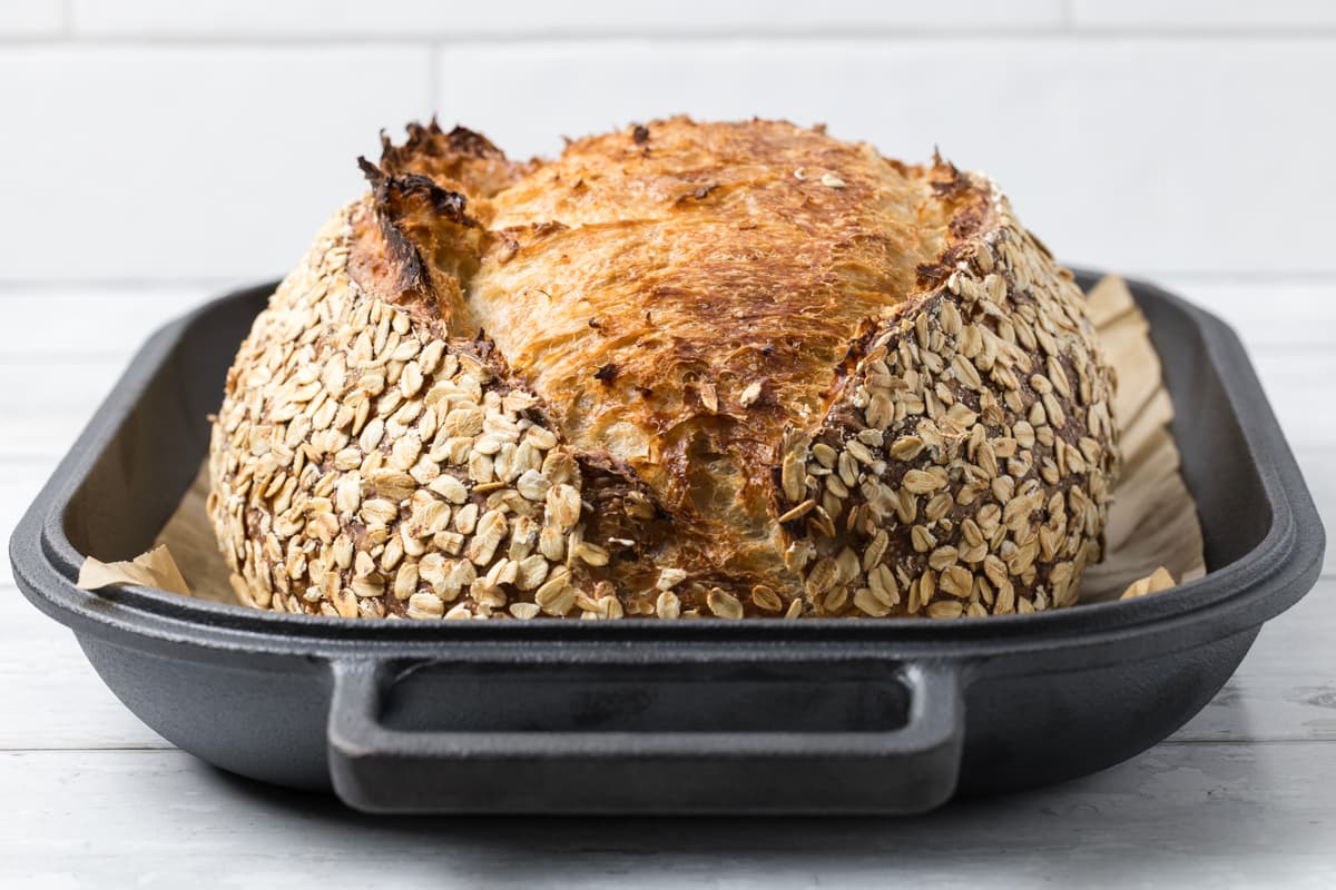 Fresh baked loaf of sourdough honey oat bread in a cast iron bread pan before being sliced.