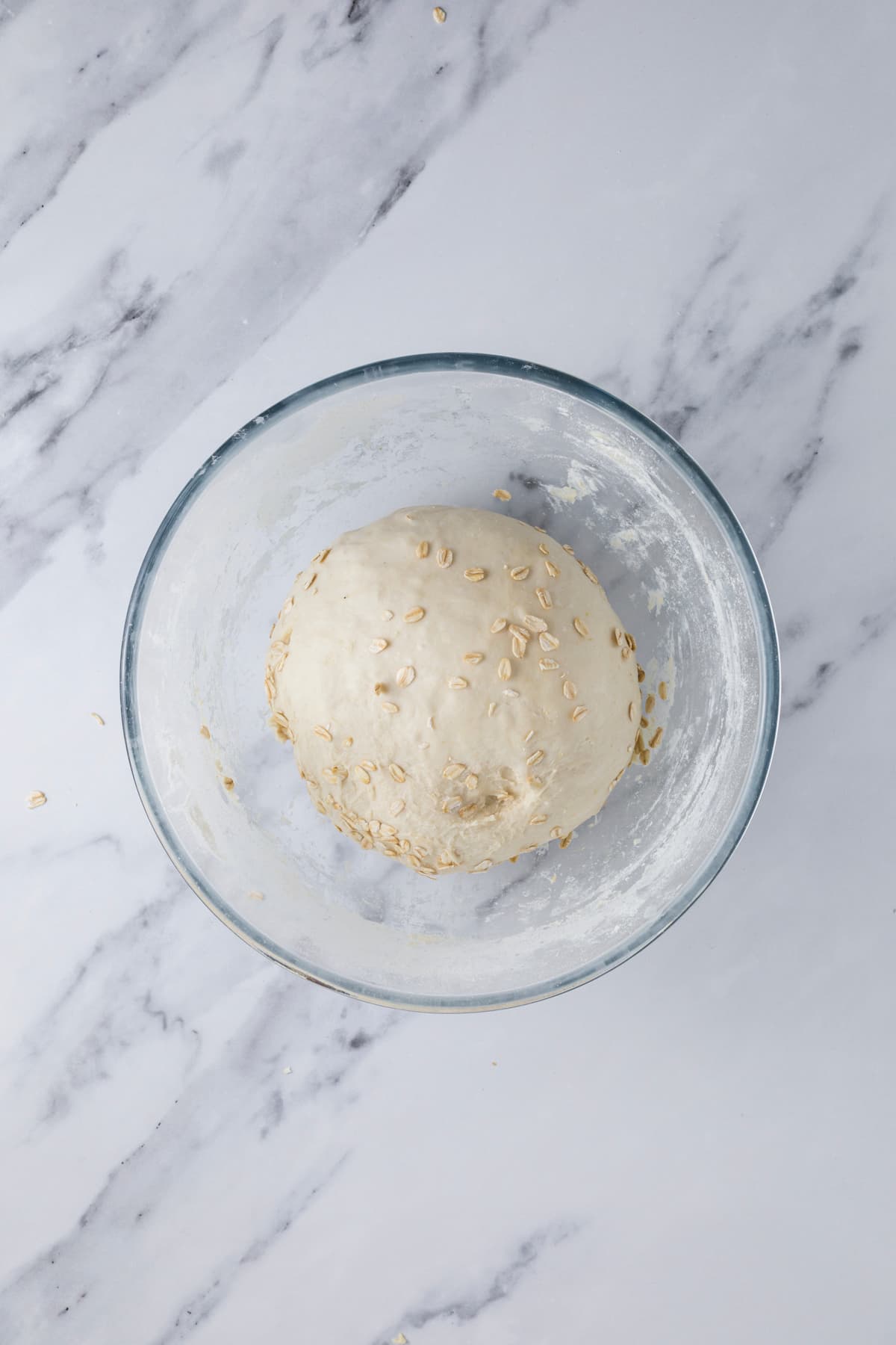 A smooth round ball of sourdough honey oat bread dough in a glass mixing bowl.