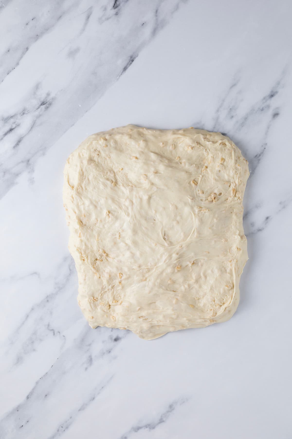 Stretching sourdough honey oat bread dough onto counter into a square shape.