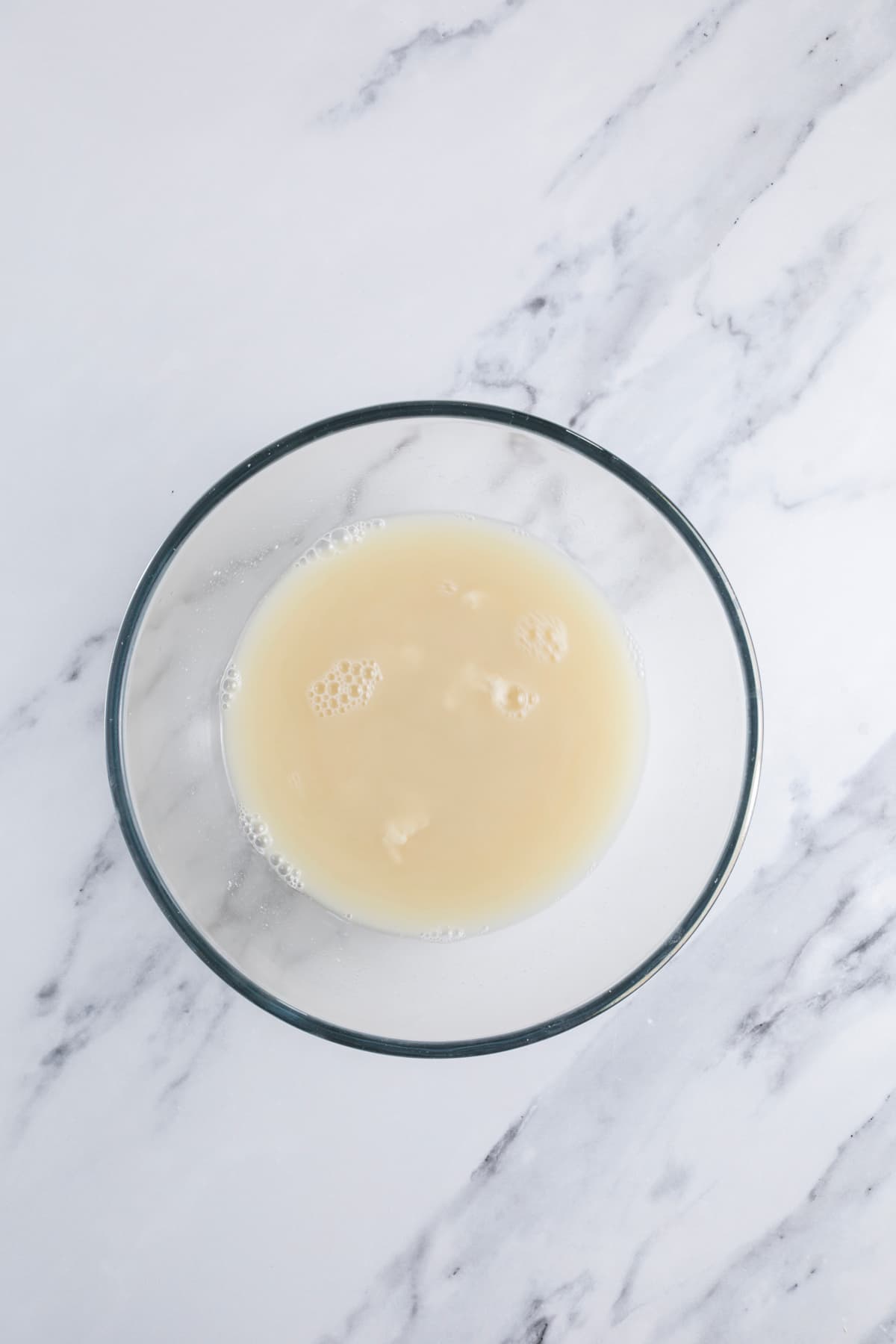 Mixing sourdough starter, water and honey in a glass bowl to make sourdough honey oat bread.