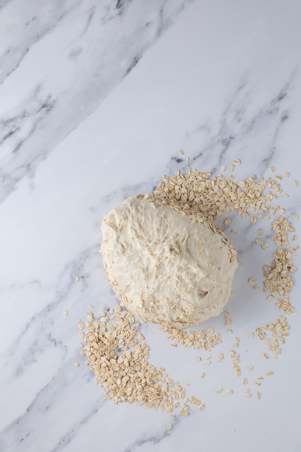 Covering sourdough honey oat bread dough with rolled oats to place in banneton.
