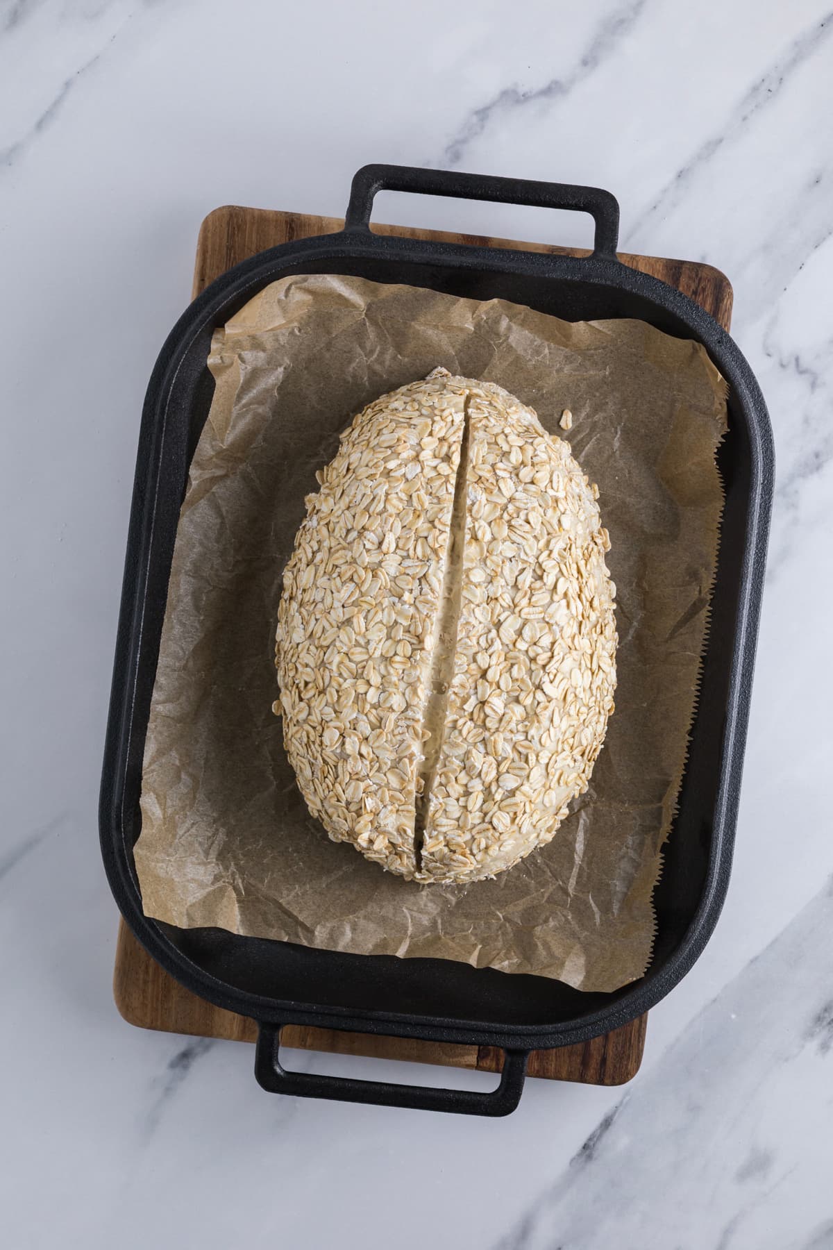 Scored bread dough in a parchment lined cast iron bread pan to bake a loaf of sourdough honey oat bread.
