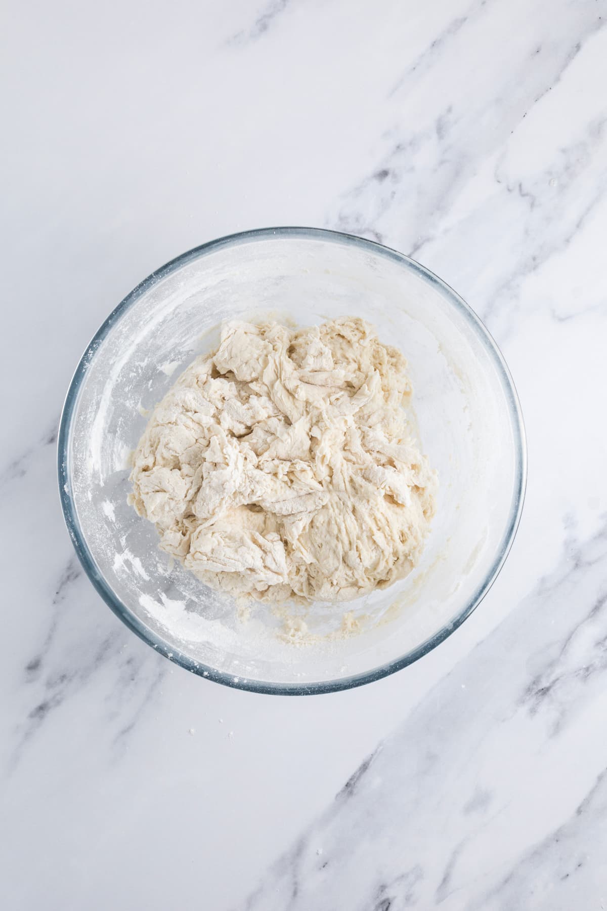 Sourdough honey oat bread dough starting to come together in a glass mixing bowl.