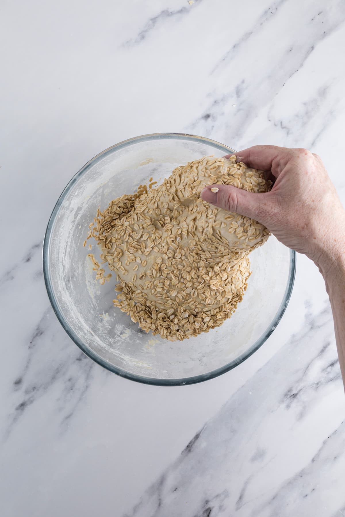 Performing stretch and folds with sourdough honey oat bread dough while mixing in rolled oats.
