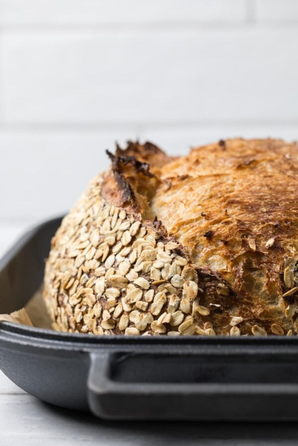 A fresh baked loaf of sourdough honey oat bread in a cast iron bread pan.