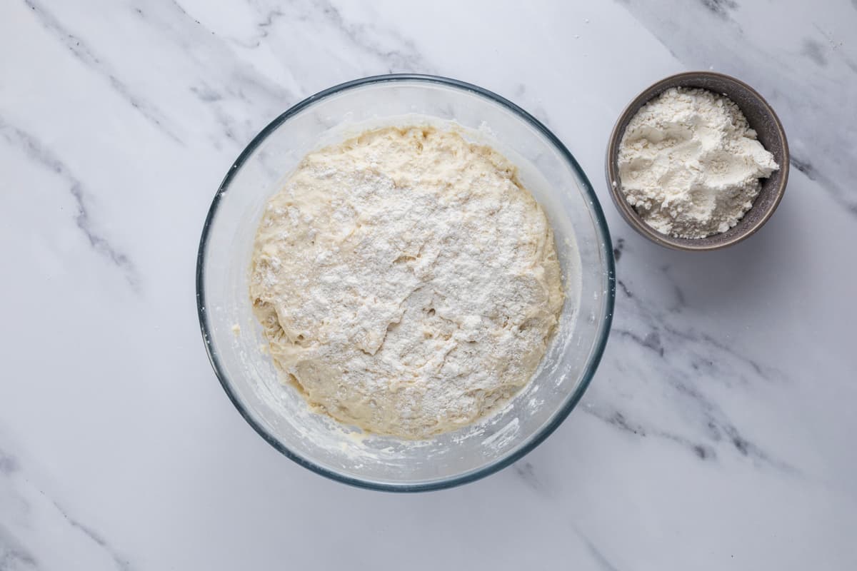 Adding rice flour to the sourdough discard roll dough before turning it out on the counter.