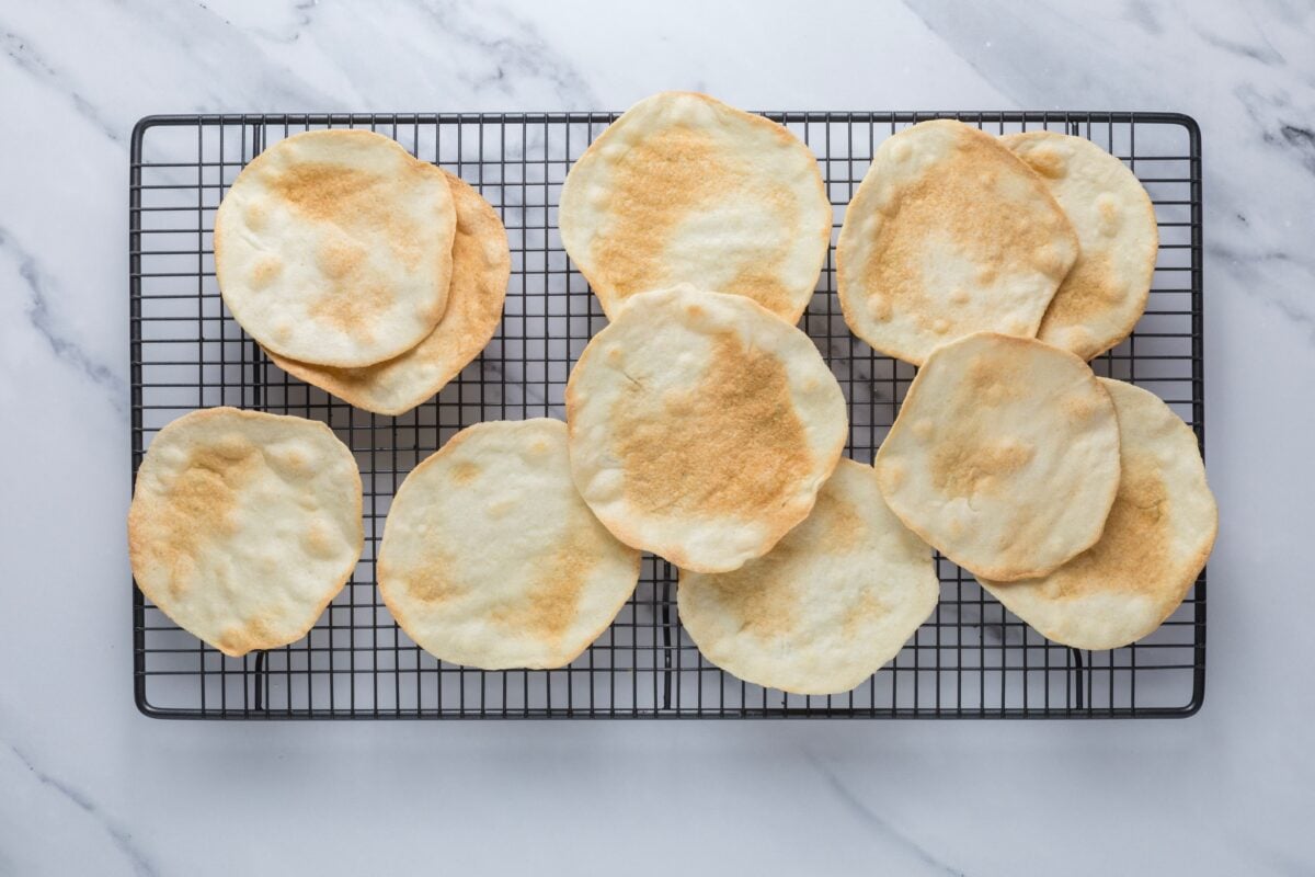 Fresh baked sourdough parchment crackers cooling on a wire rack.