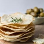 A stack of sourdough parchment crackers on a serving tray with a bowl of olives in the background.