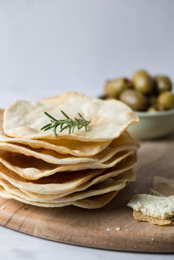 A stack of sourdough parchment crackers on a serving tray with a bowl of olives in the background.