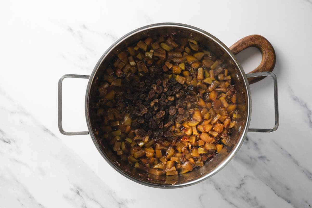 Adding raisins to a pot of cooking peach chutney.