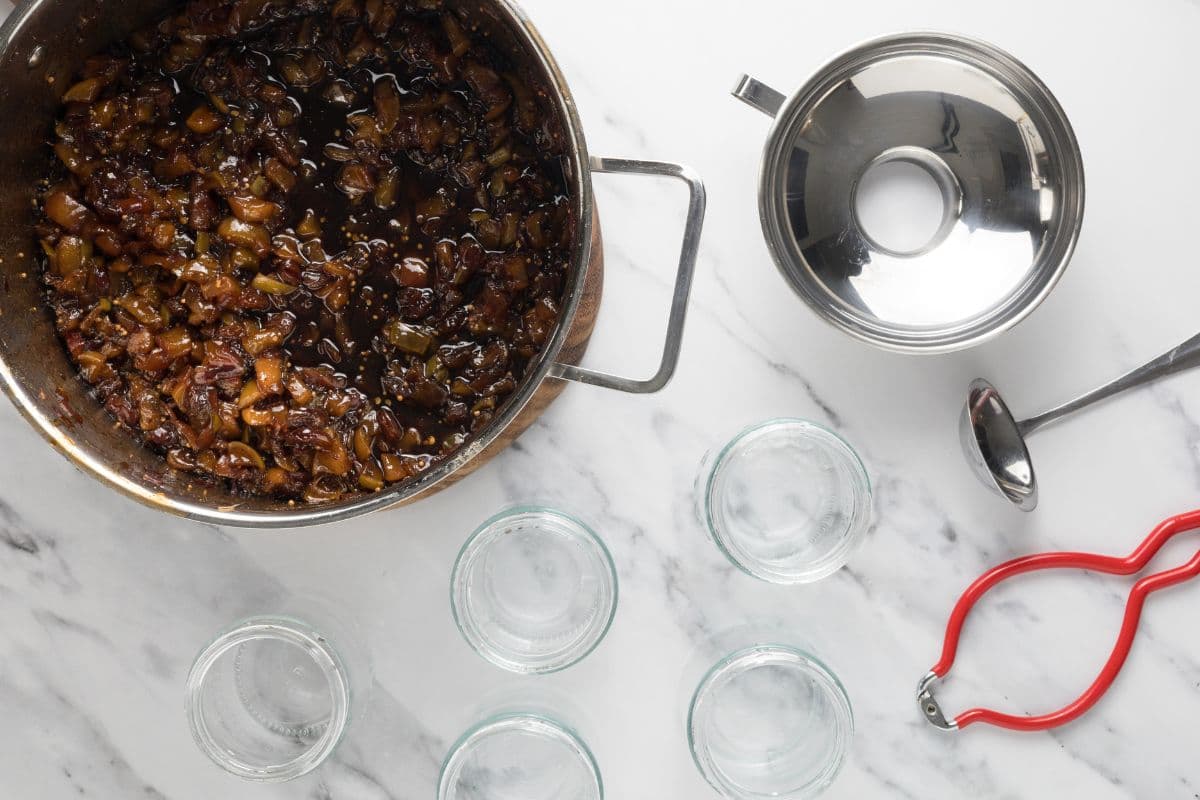 A pot of peach chutney next to storage jars with a meta funnel so peach chutney can be added to jars.