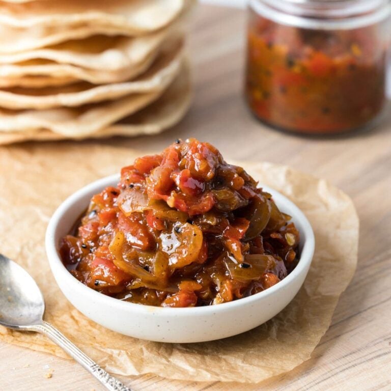 A bowl of red pepper relish sitting in front of sourdough crackers.