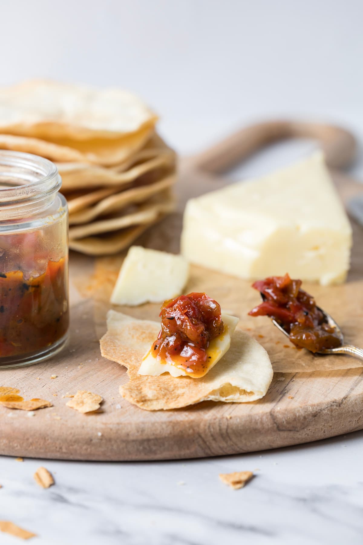 Red pepper relish served on top of a piece of cheese on top of a sourdough cracker.