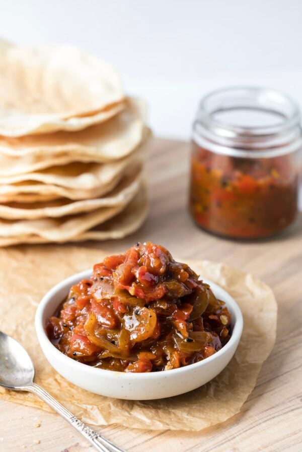 A bowl of red pepper relish on a serving board with sourdough crackers.