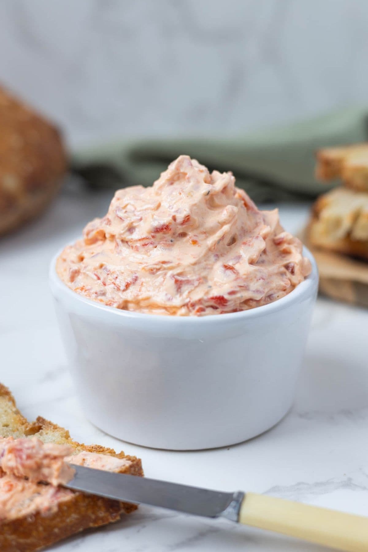 A small bowl of roasted red pepper cream cheese dip being served with sourdough toast.
