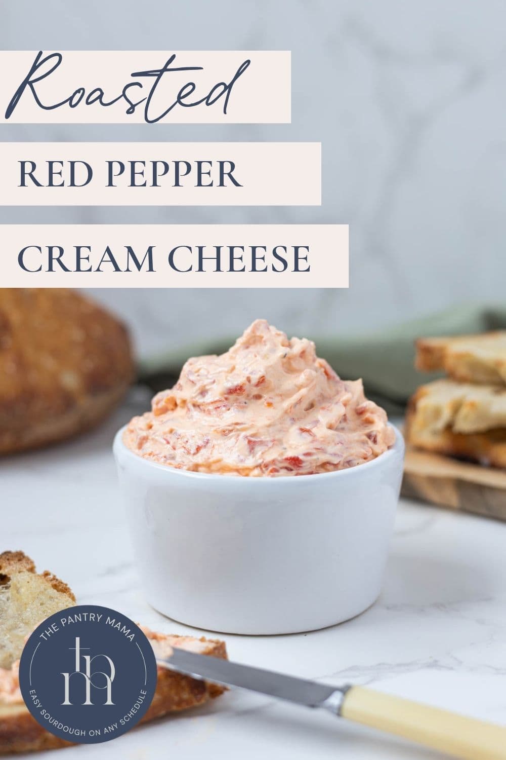 Roasted red pepper cream cheese dip in a bowl with text overlay and sourdough bread on the side.