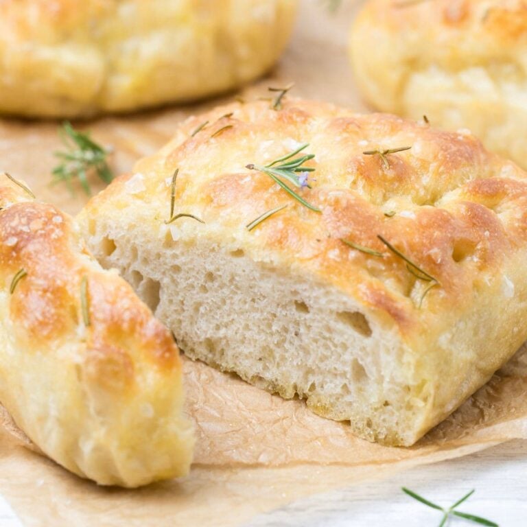 Close up image of a sliced loaf of simple sourdough focaccia bread topped with rosemary leaves.