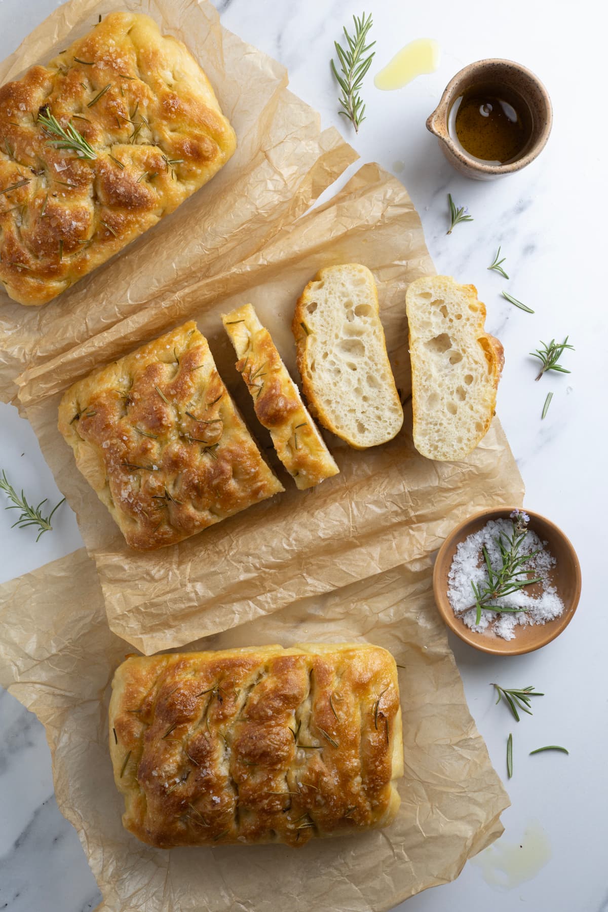 Three loaves of simple sourdough focaccia bread on parchment paper with one loaf sliced open to show inside texture.