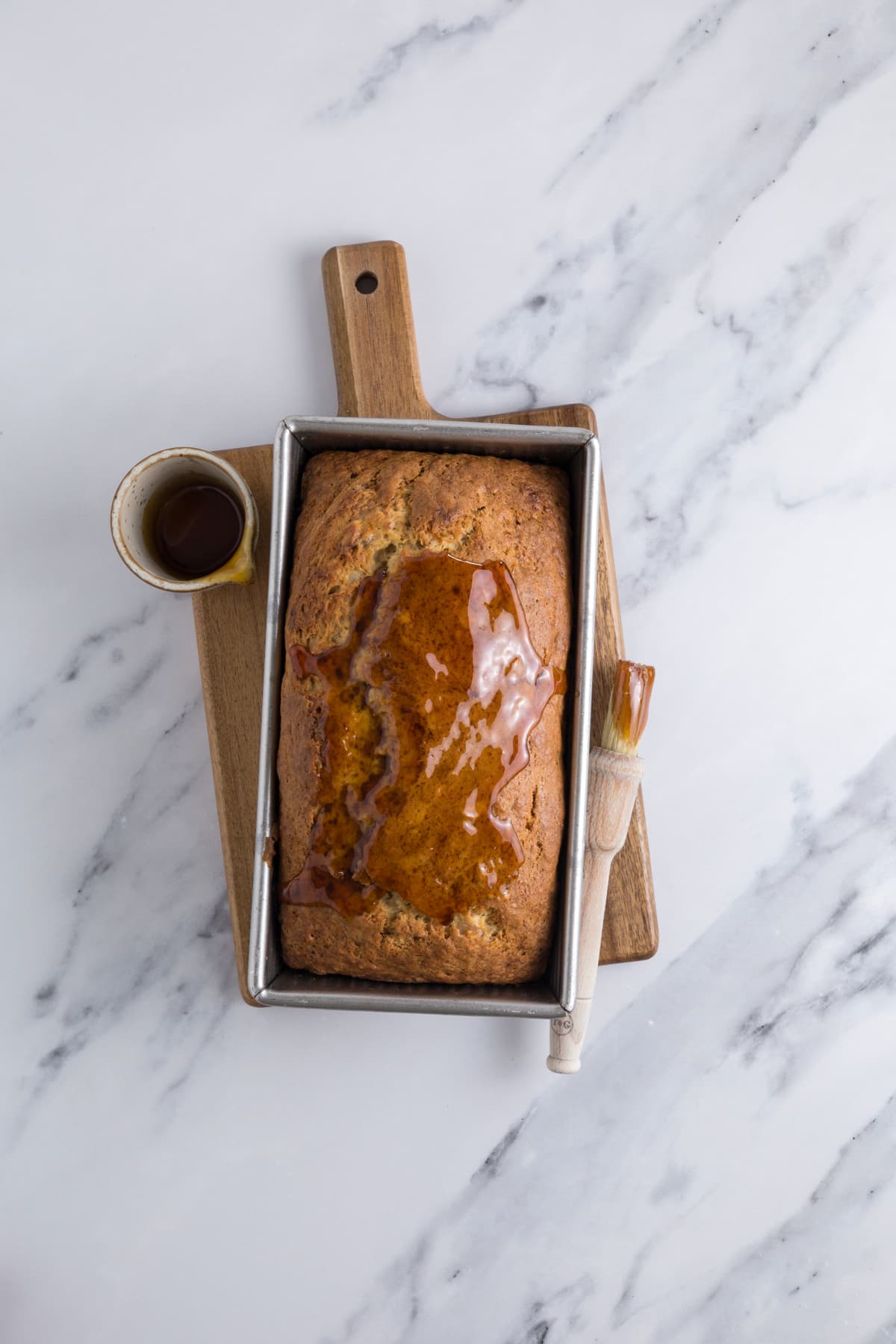 Adding golden syrup to the top of a fresh baked loaf of sourdough discard banana bread.