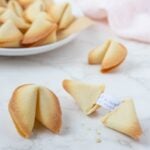 Close up of a sourdough fortune cookie on the counter with one broken open to show a fortune inside.
