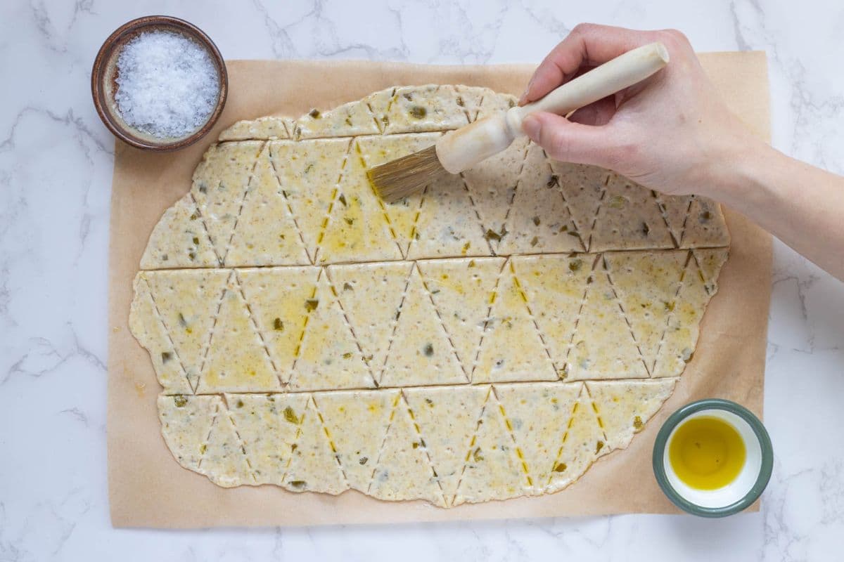Brushing the rolled out sourdough jalapeño cheddar cracker dough with oil just before baking.