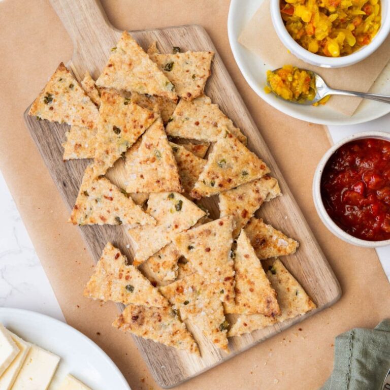 A wooden board with a pile of sourdough jalapeño cheddar crackers for serving with relish and cut cheese.