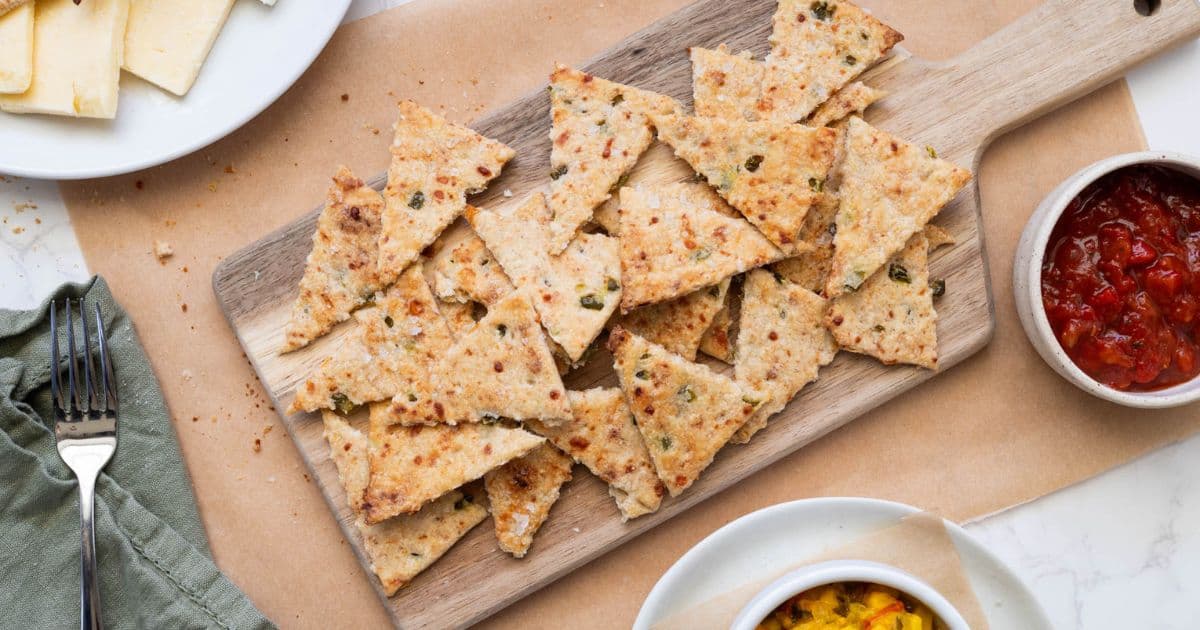 A board with sourdough jalapeño cheddar crackers being served with cheese, tomato relish and corn relish.