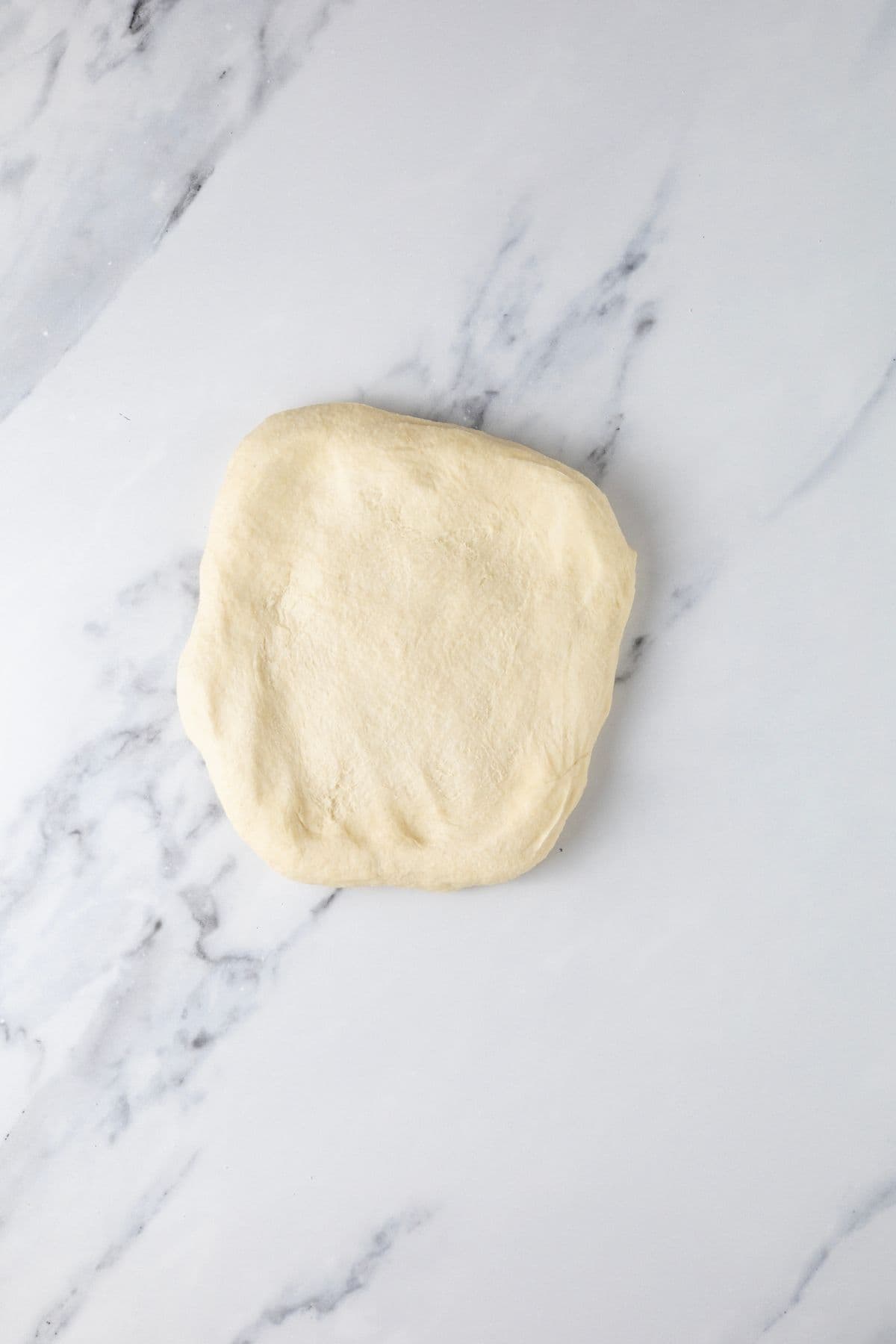 A stretched out ball of sourdough parchment cracker dough on the counter to be divided into cracker pieces.