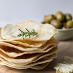 Close up of a stack of sourdough parchment crackers with a sprig of rosemary on top for serving.