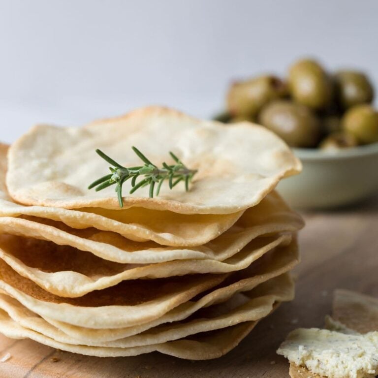 Close up of a stack of sourdough parchment crackers with a sprig of rosemary on top for serving.