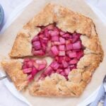 A sourdough rhubarb galette on a piece of parchment paper being sliced for serving.