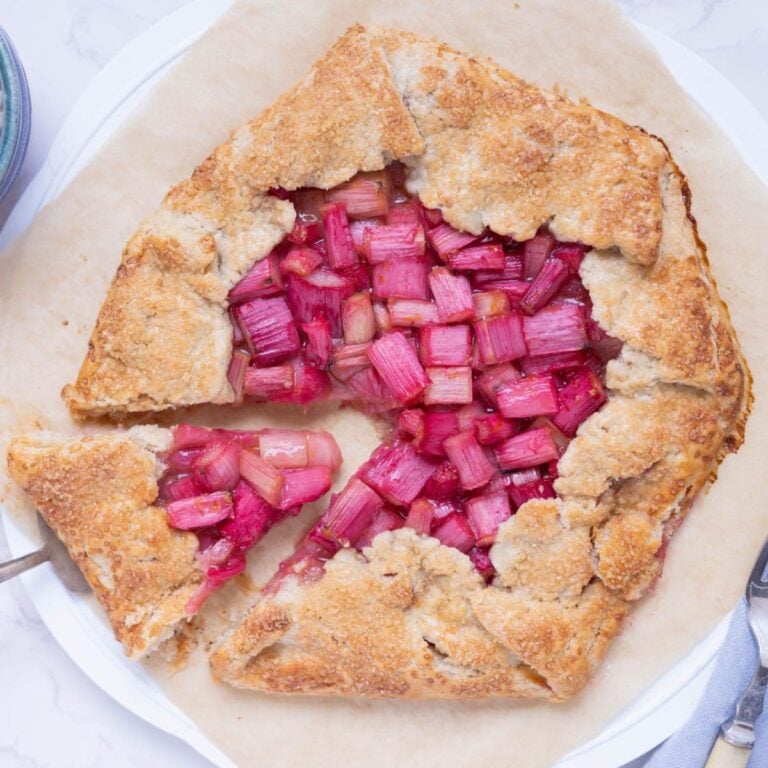 A sourdough rhubarb galette on a piece of parchment paper being sliced for serving.