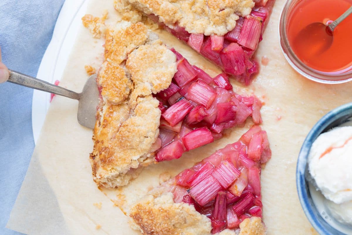 A close up of a slice of sourdough rhubarb galette next to a jar of rhubarb syrup and vanilla ice cream.
