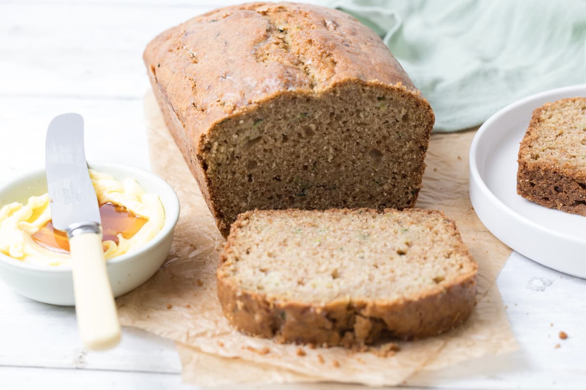 Slicing a loaf of sourdough zucchini bread and serving on a plate with honey butter.