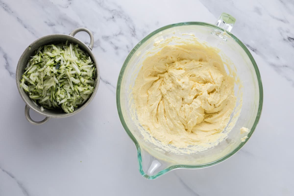 Wet and dry ingredients for sourdough zucchini bread mixed together next to a bowl of shredded zucchini.