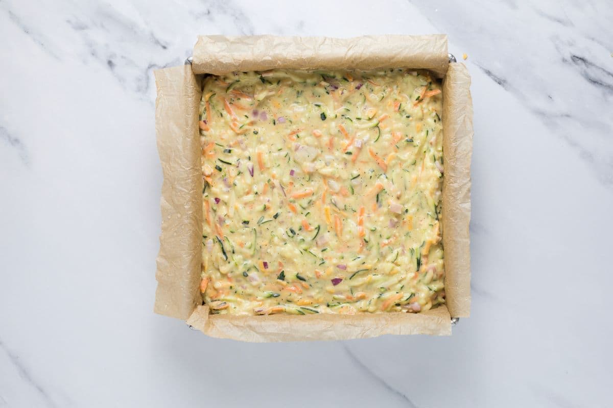 Sourdough zucchini slice batter in a parchment lined baking dish.