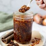 Jar of homemade chili crunch oil with crispy garlic and chili flakes on a spoon.
