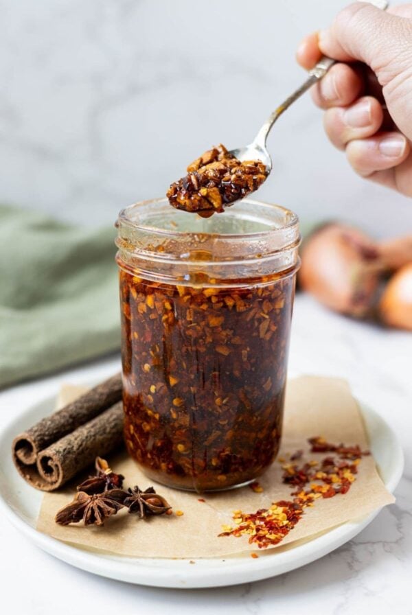 Jar of homemade chili crunch oil with crispy garlic and chili flakes on a spoon.