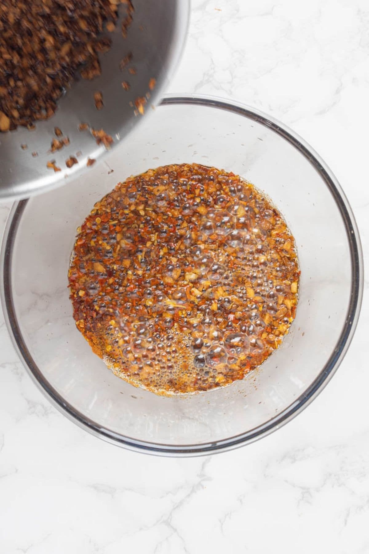 Pouring hot oil, shallots, and garlic over chili flakes to make homemade chili crunch oil.