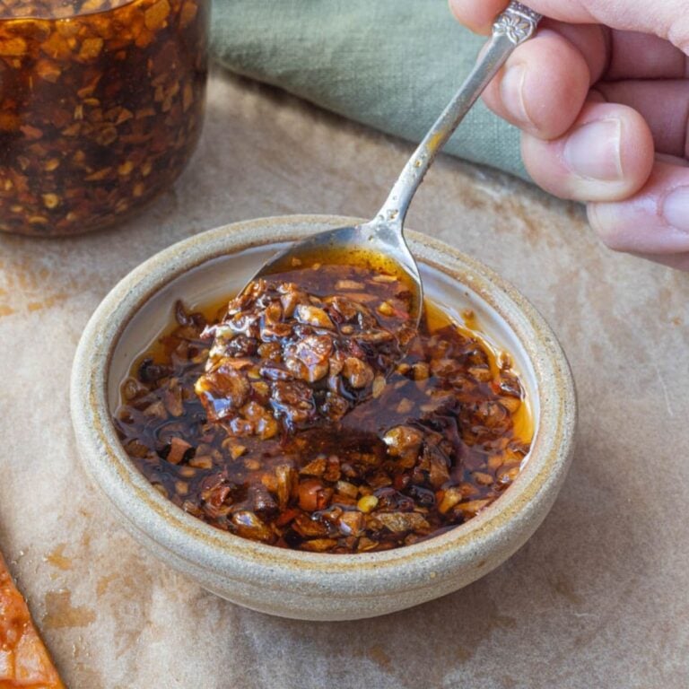 Close up of homemade chili crunch oil in a bowl with crispy garlic pieces and chili flakes.