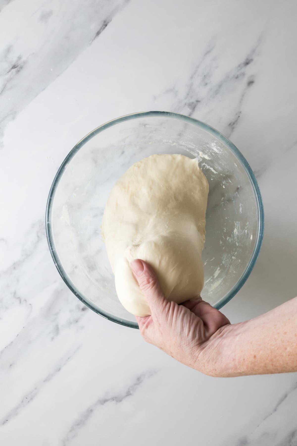 Hand lifting overnight sourdough bread dough from a mixing bowl during stretch and folds.