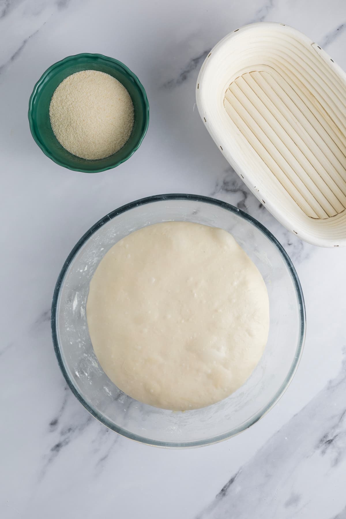 Overnight sourdough bread dough after bulk fermentation beside a banneton just before shaping.