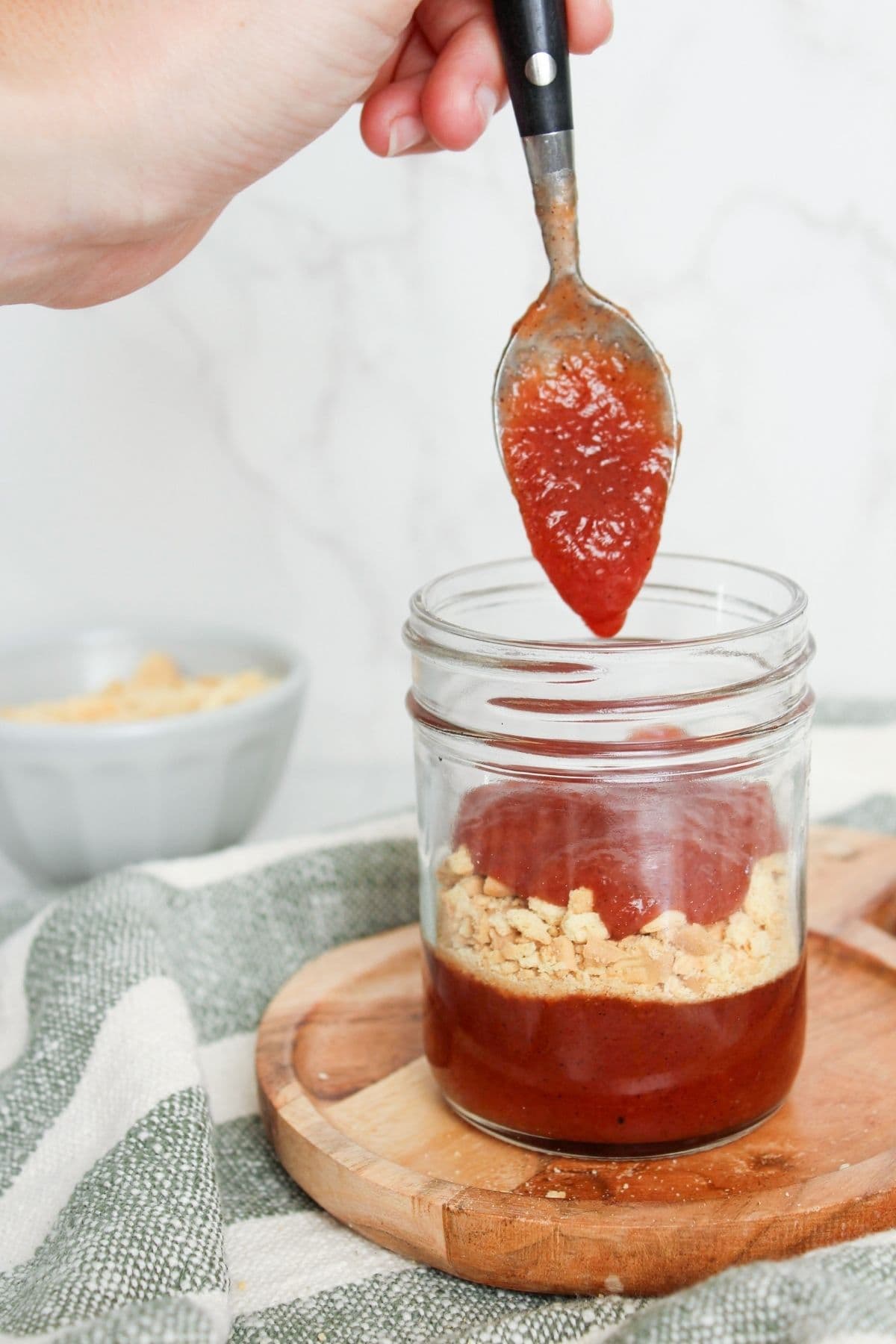 Spoonful of peach cobbler jam being layered into a glass jar over crushed shortbread cookies.